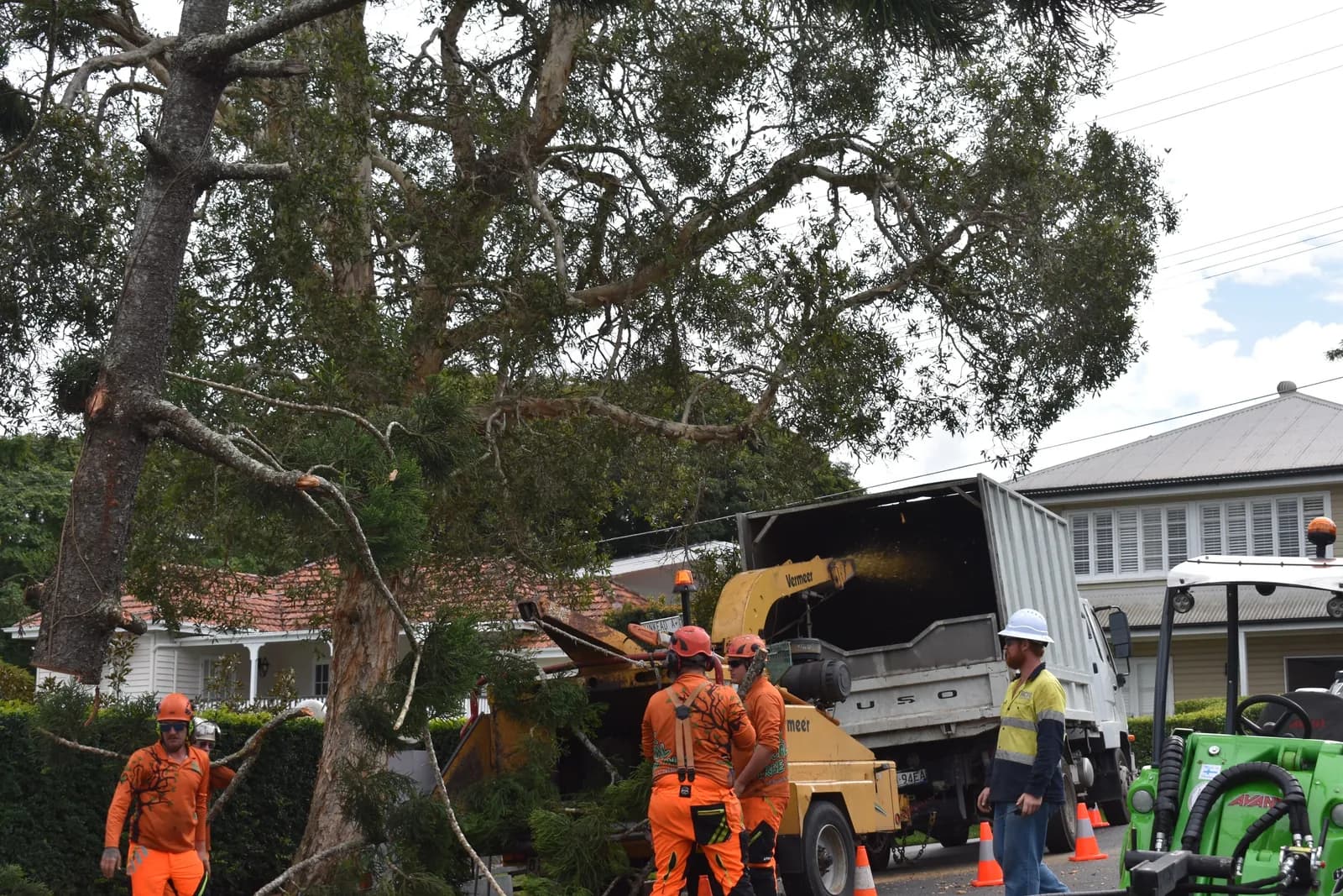 Two arborists working the chipper as the ground crew clears